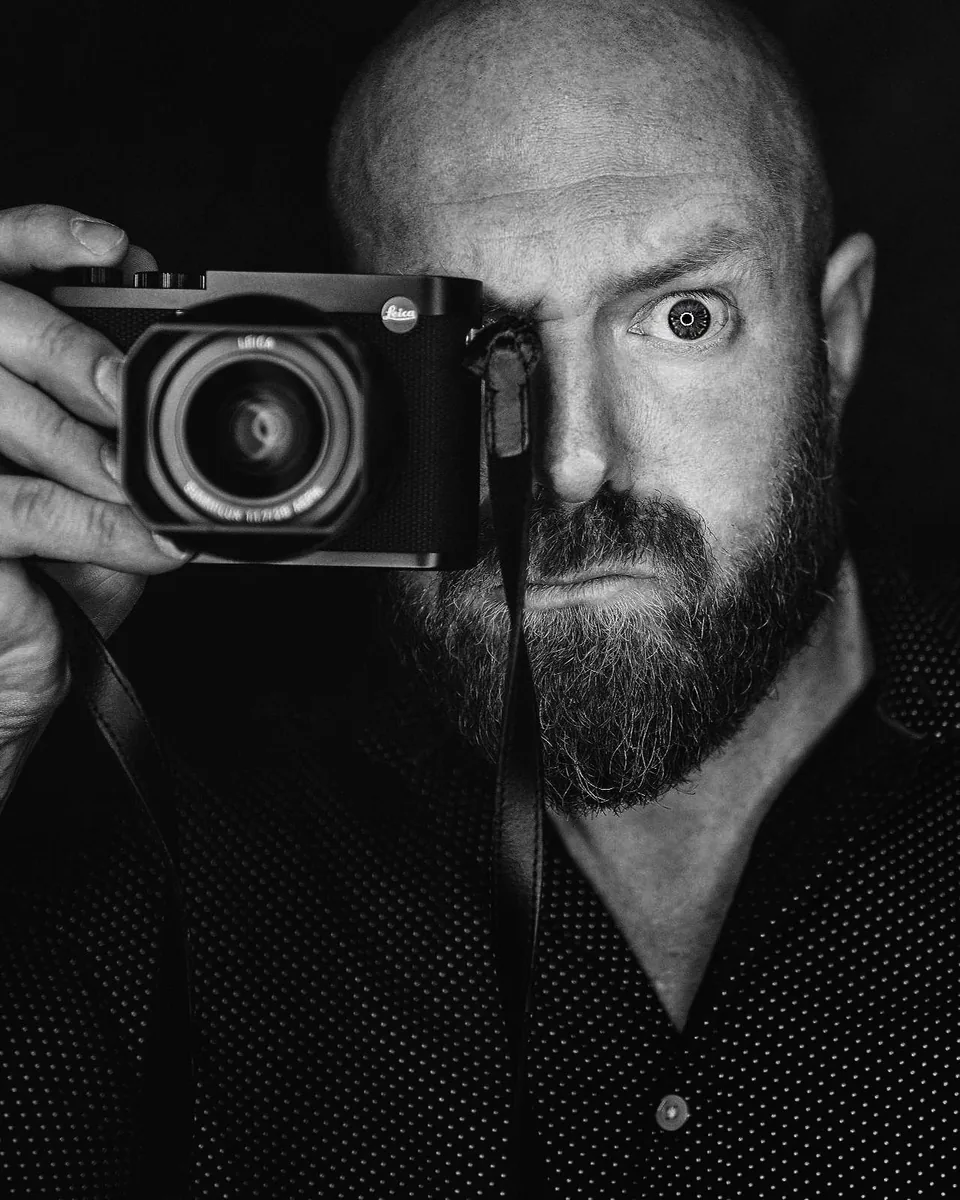 Black-and-white portrait of wedding photographer Jay Cassario holding his Leica camera up to one eye