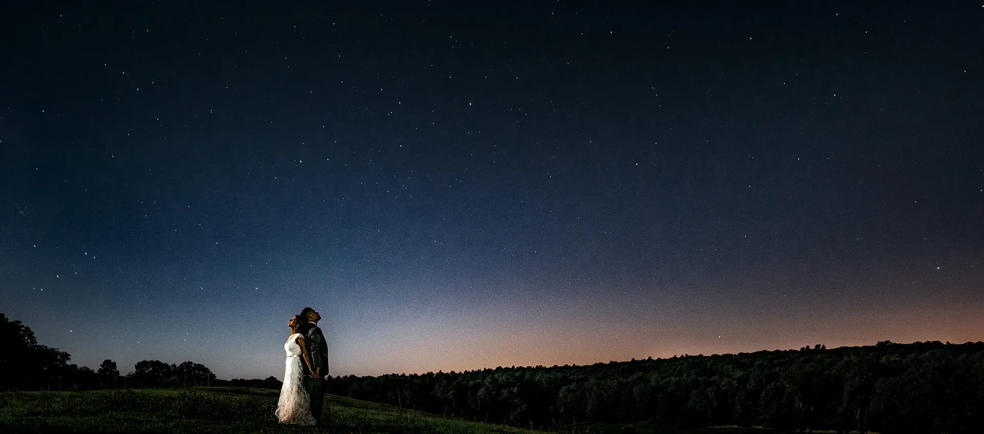 Bride and groom leaning back to back under a starry night sky