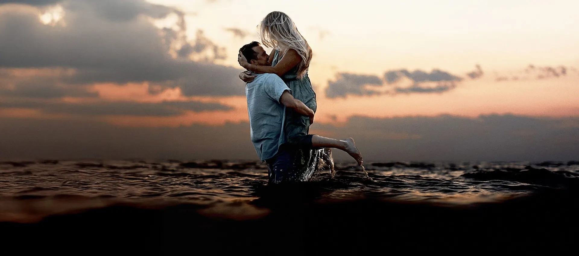 Couple embracing waist-deep in the ocean at sunset during their Cape May, New Jersey engagement session