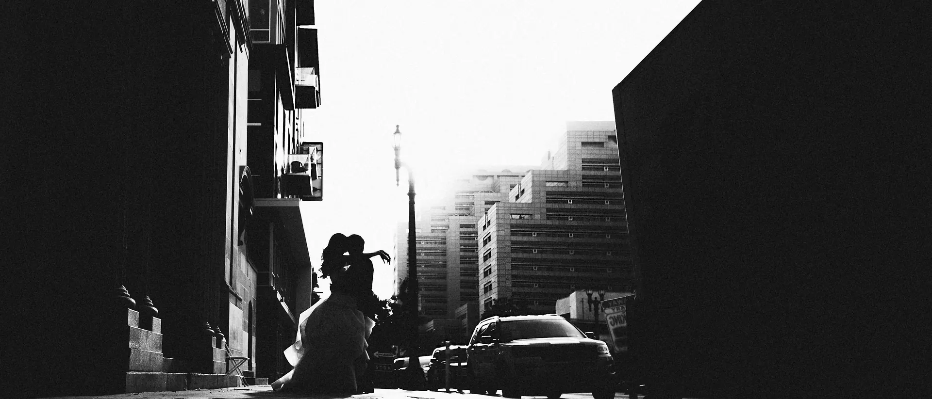 Black and white silhouette of a bride and groom kissing on a sunlit street in downtown Los Angeles