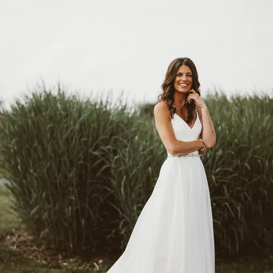 Smiling bride in a flowing gown standing in front of tall grasses