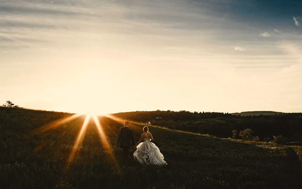 Bride and groom walking hand in hand through a hillside field at sunset in Lancaster, Pennsylvania