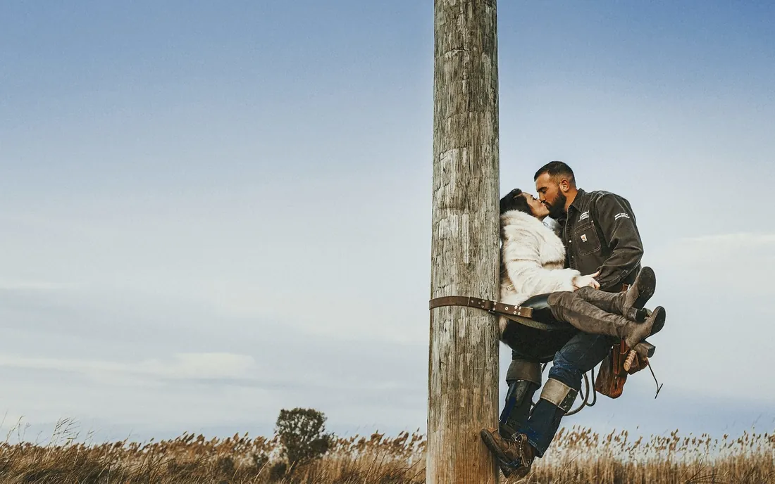 Playful engaged couple climbing a wooden pole by a marsh