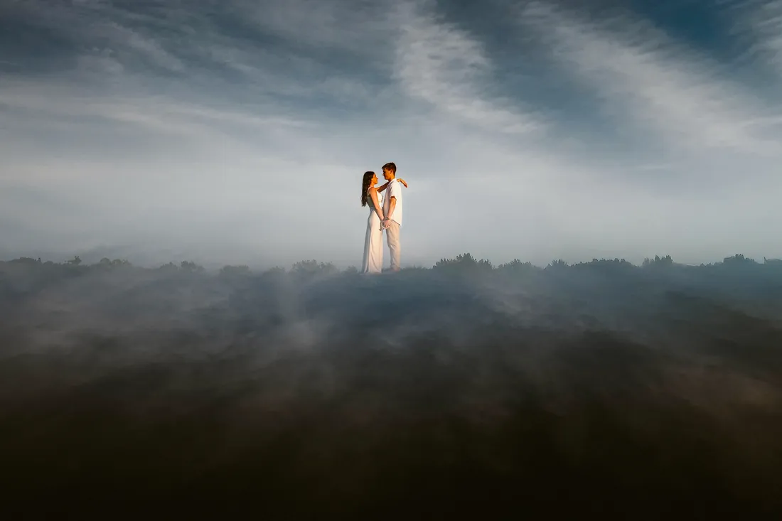 Engaged couple standing above a sea of clouds