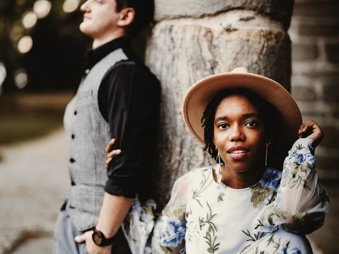 Engaged couple by a stone column, the woman in a wide-brimmed hat