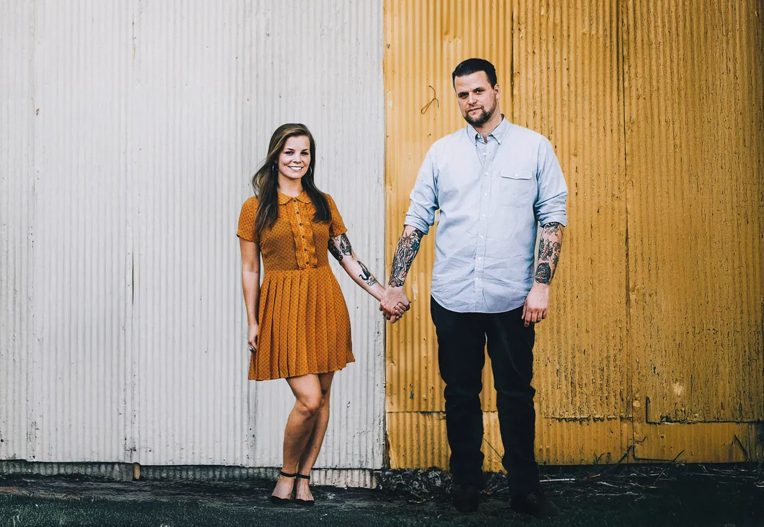 Engaged couple holding hands in front of a yellow door
