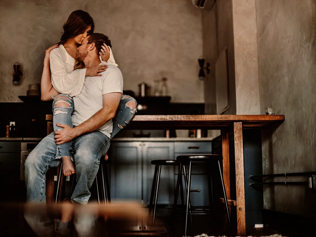 Engaged couple embracing on a stool in a rustic kitchen