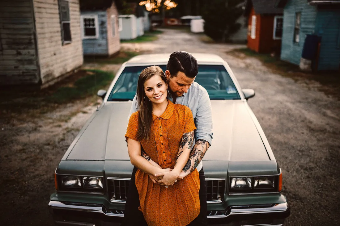 Engaged couple leaning on a vintage car in a narrow lane
