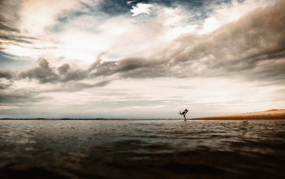 Engaged couple small on the shoreline under a dramatic sky