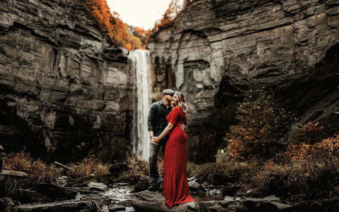 Engaged couple in front of a tall waterfall in a rocky gorge