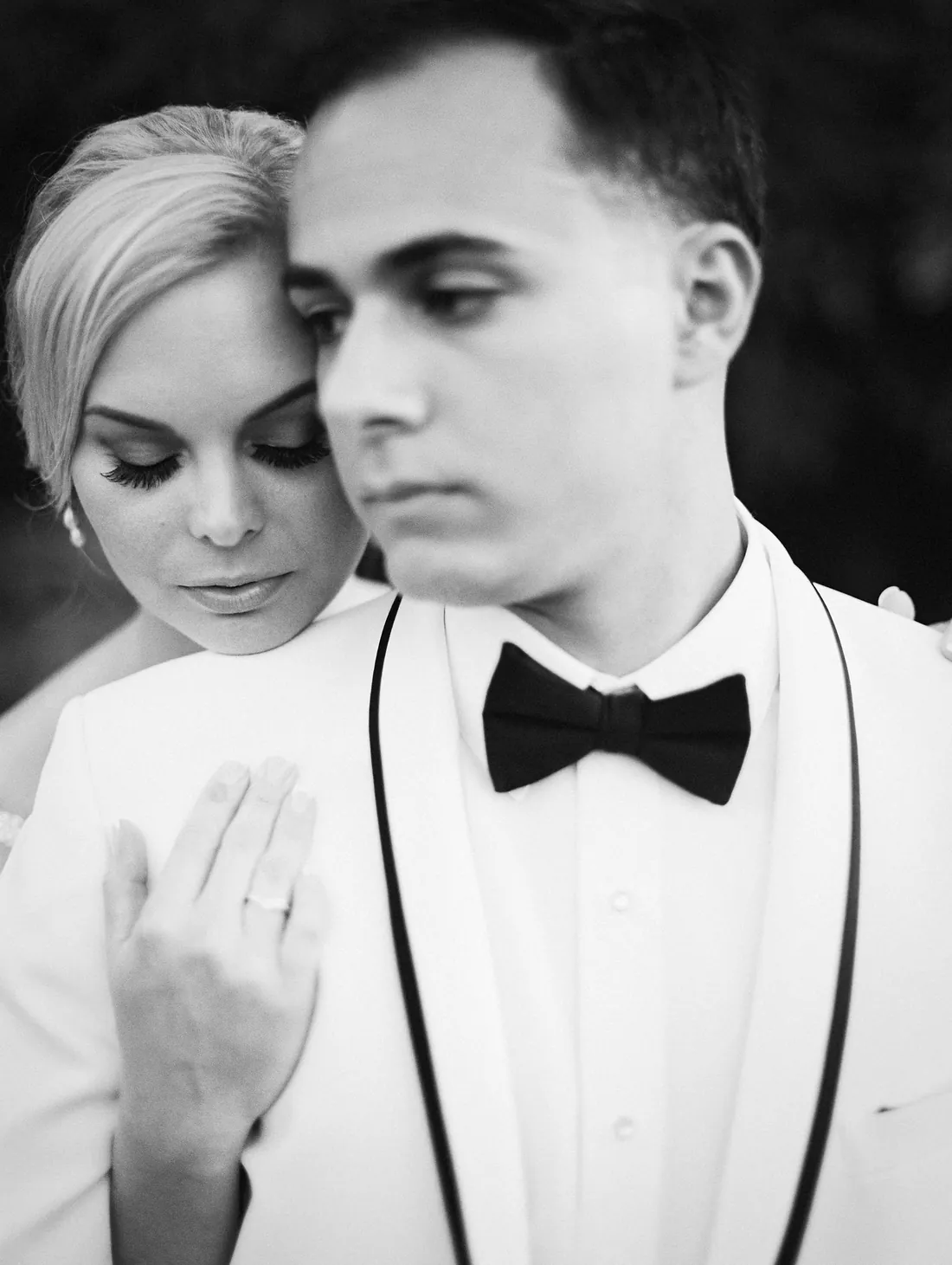 Black and white film portrait of a bride resting against her groom