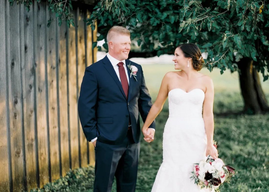 Film photograph of a bride and groom holding hands by a wooden fence