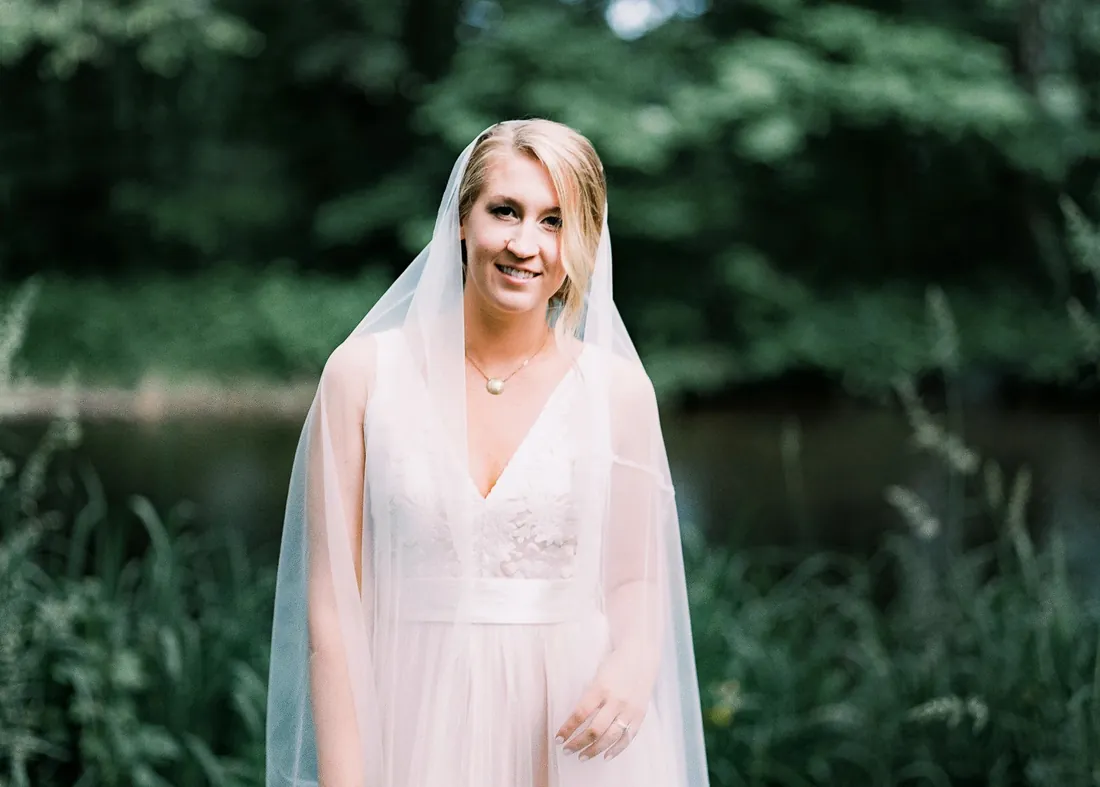 Film portrait of a smiling bride in a long veil by the water