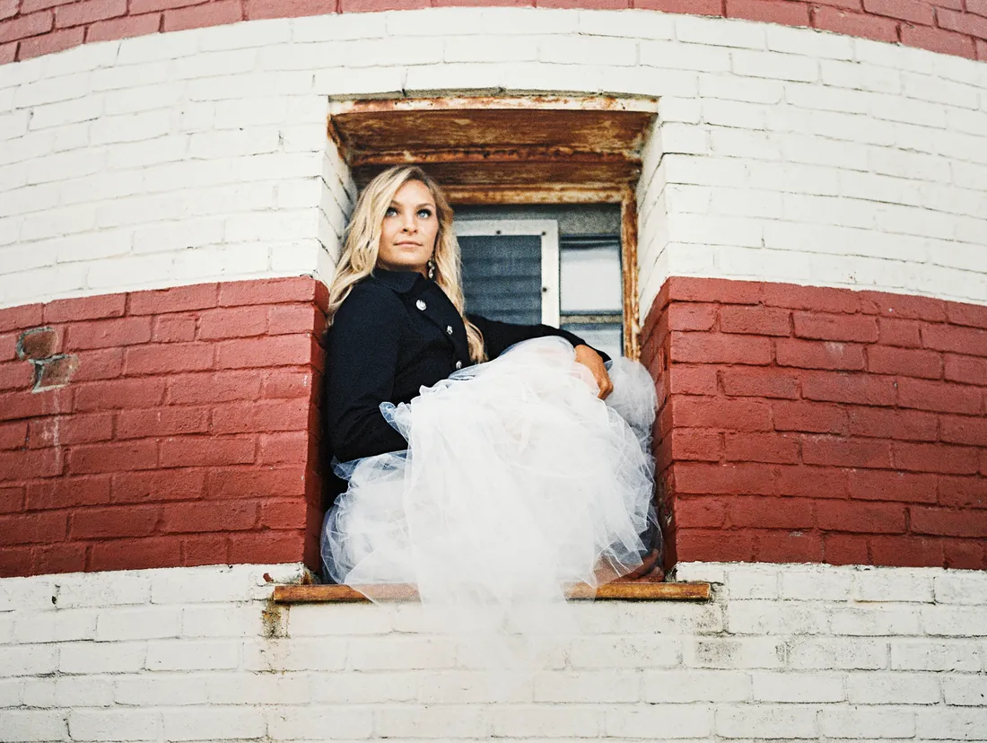 Film photograph of a bride sitting in the window of a red and white lighthouse