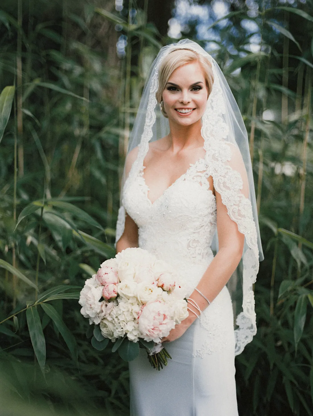 Film portrait of a smiling bride in a lace cathedral veil holding peonies