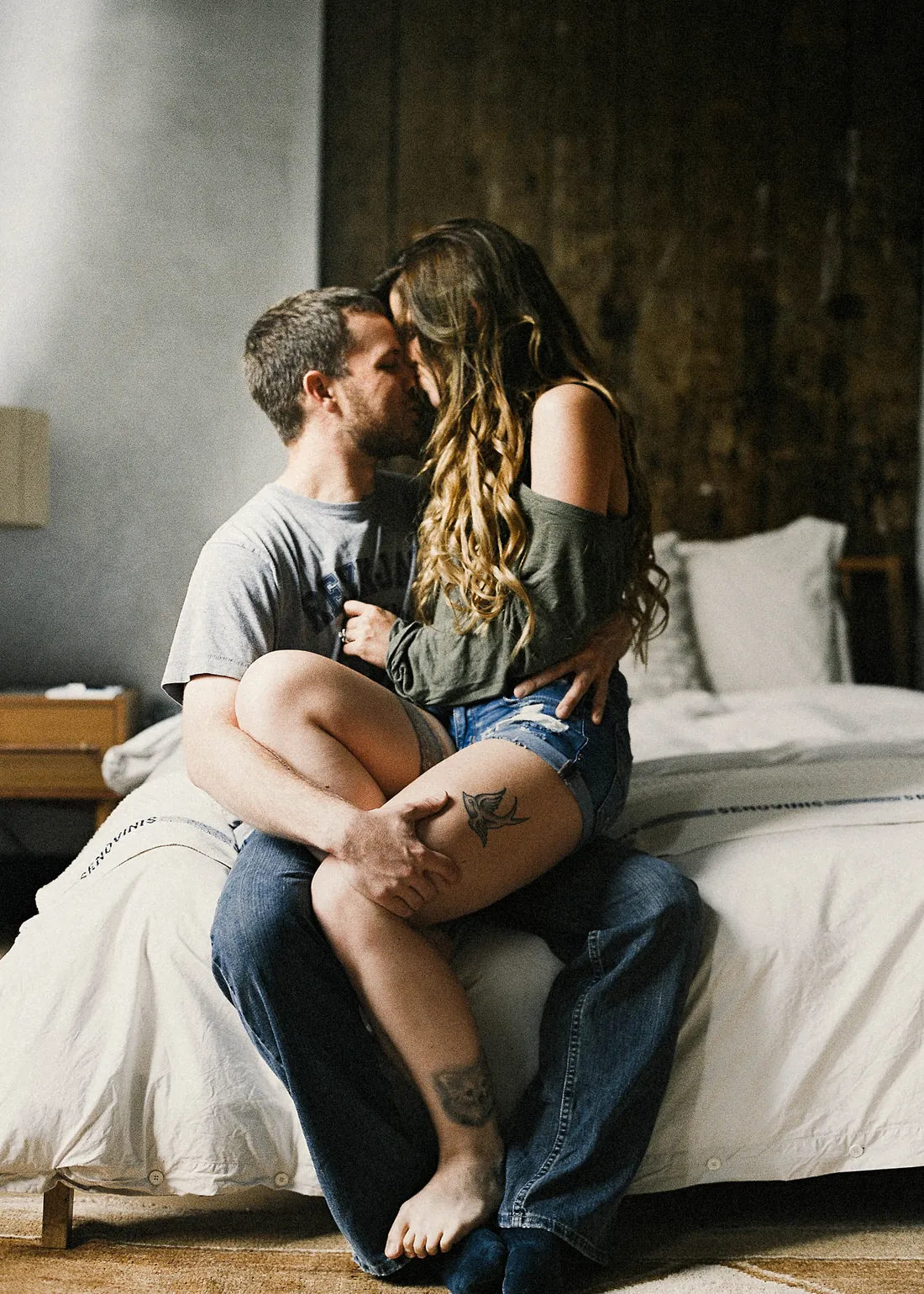 Film photograph of an engaged couple embracing on the edge of a bed at home