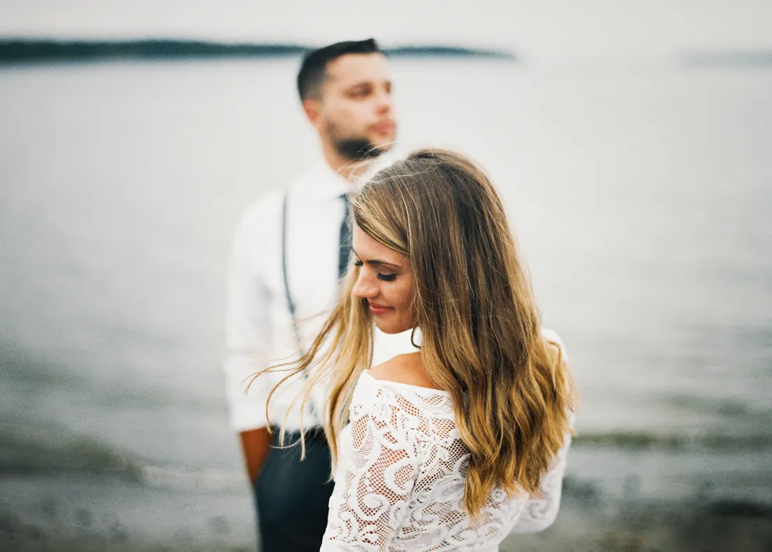 Film photograph of a couple by the water, the woman looking down and smiling