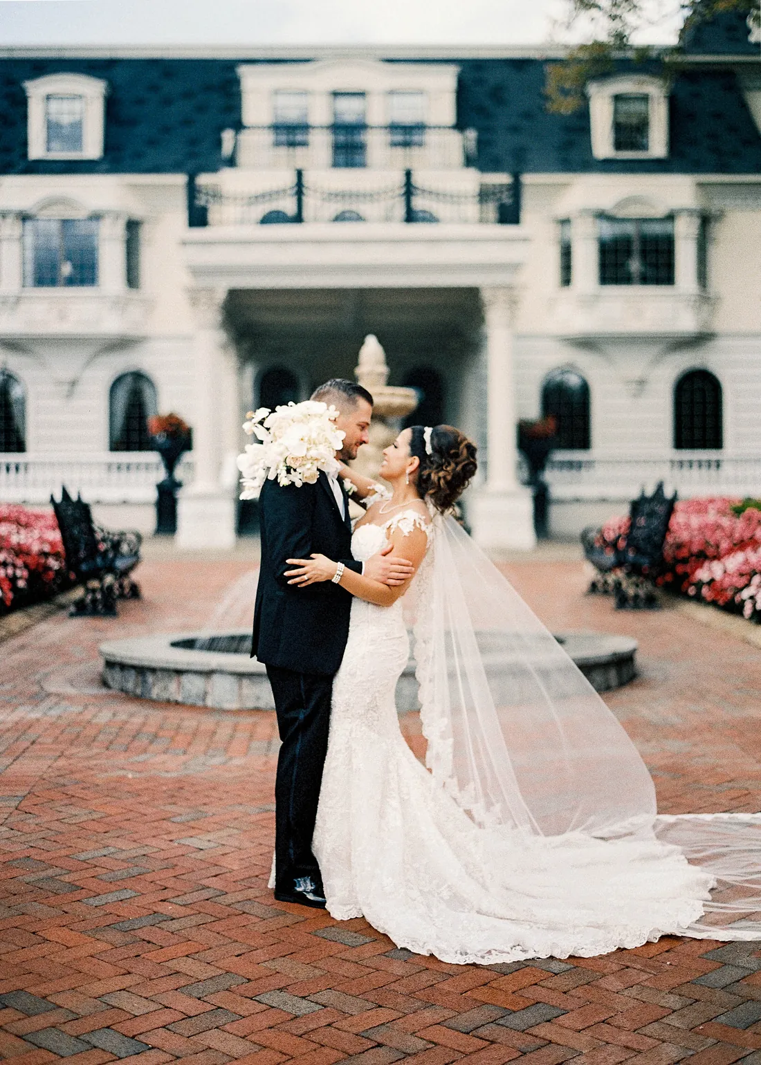 Film photograph of a bride and groom kissing in a brick courtyard in front of a mansion