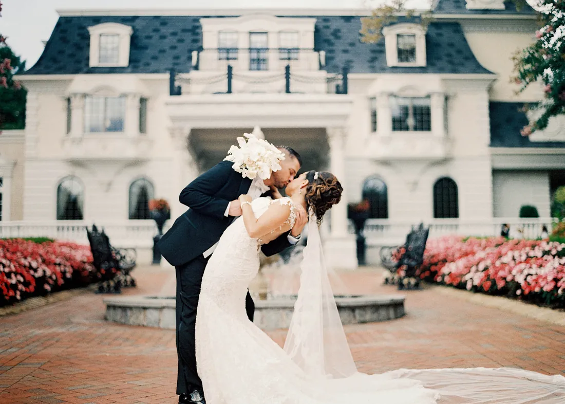 Film photograph of a groom dipping his bride for a kiss in front of a white mansion