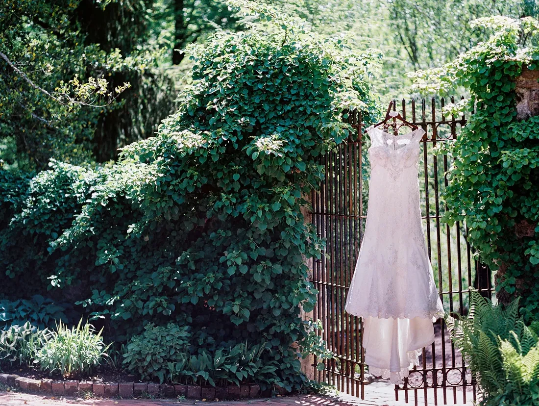 Film photograph of a wedding dress hanging on an iron garden gate
