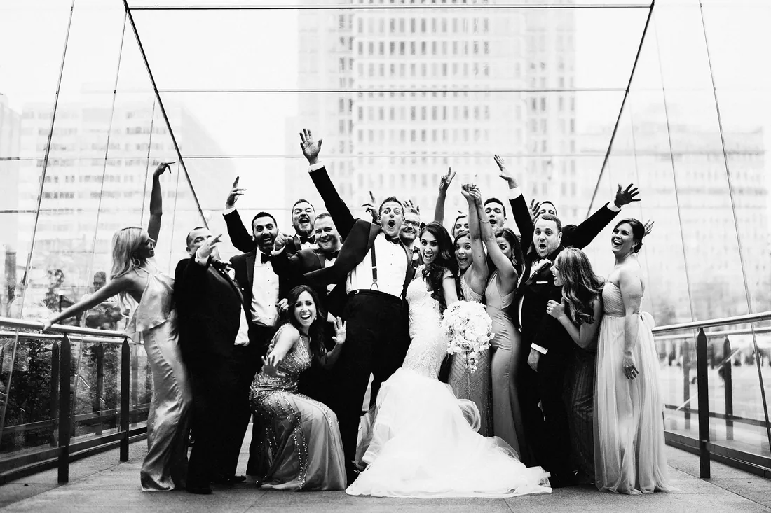 Black and white photo of a bridal party cheering on a city footbridge