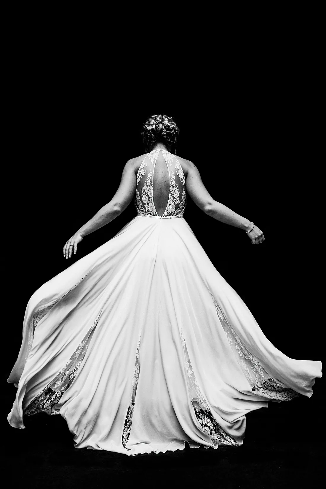 Black and white photo of a bride's flowing gown against a black background