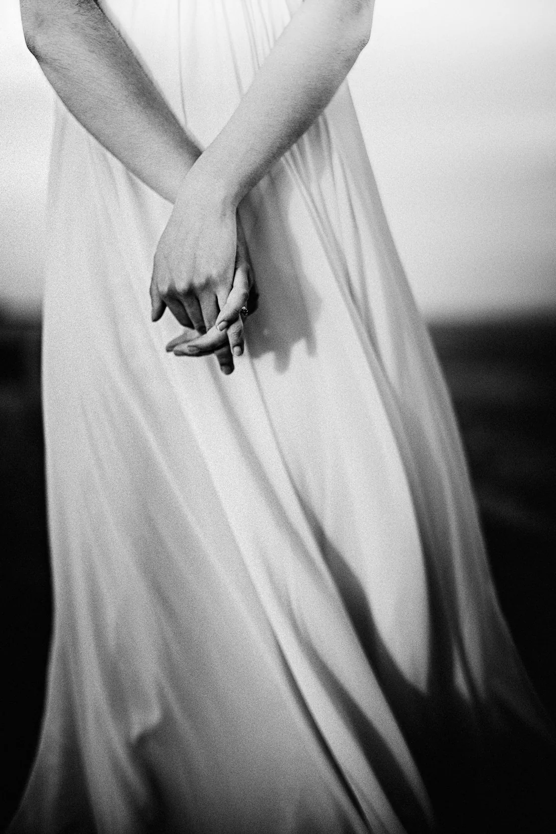 Black and white detail of a bride's hands holding her flowing skirt