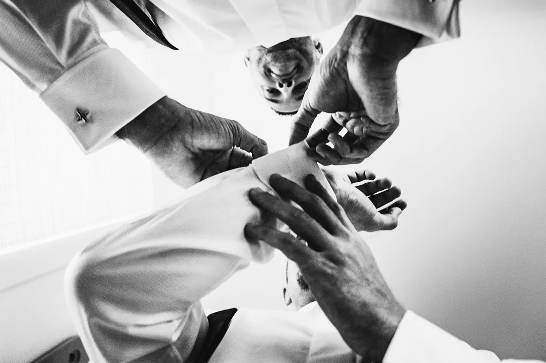 Black and white photo of hands fastening a groom's cufflinks