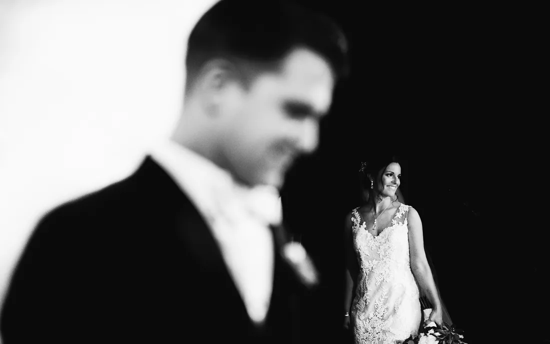 Black and white photo of a groom smiling as his bride approaches