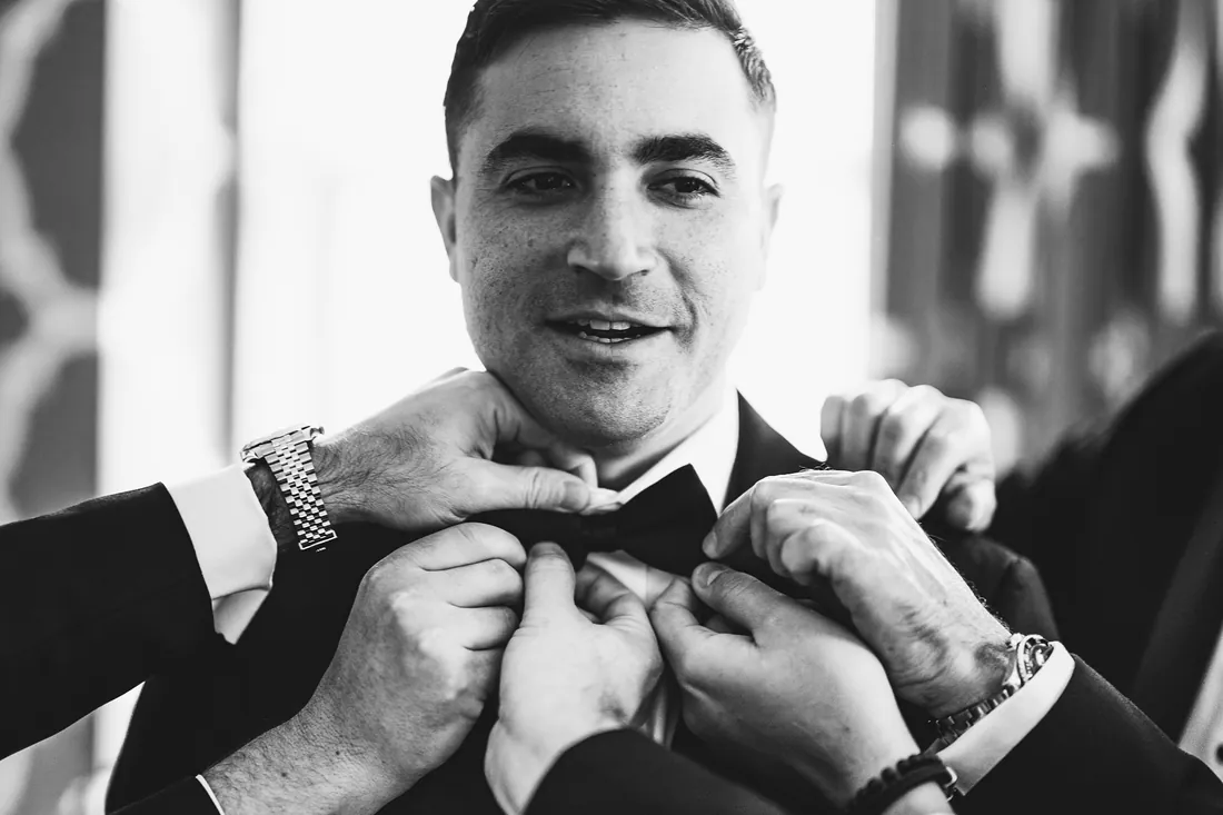 Black and white photo of groomsmen fixing the groom's bow tie