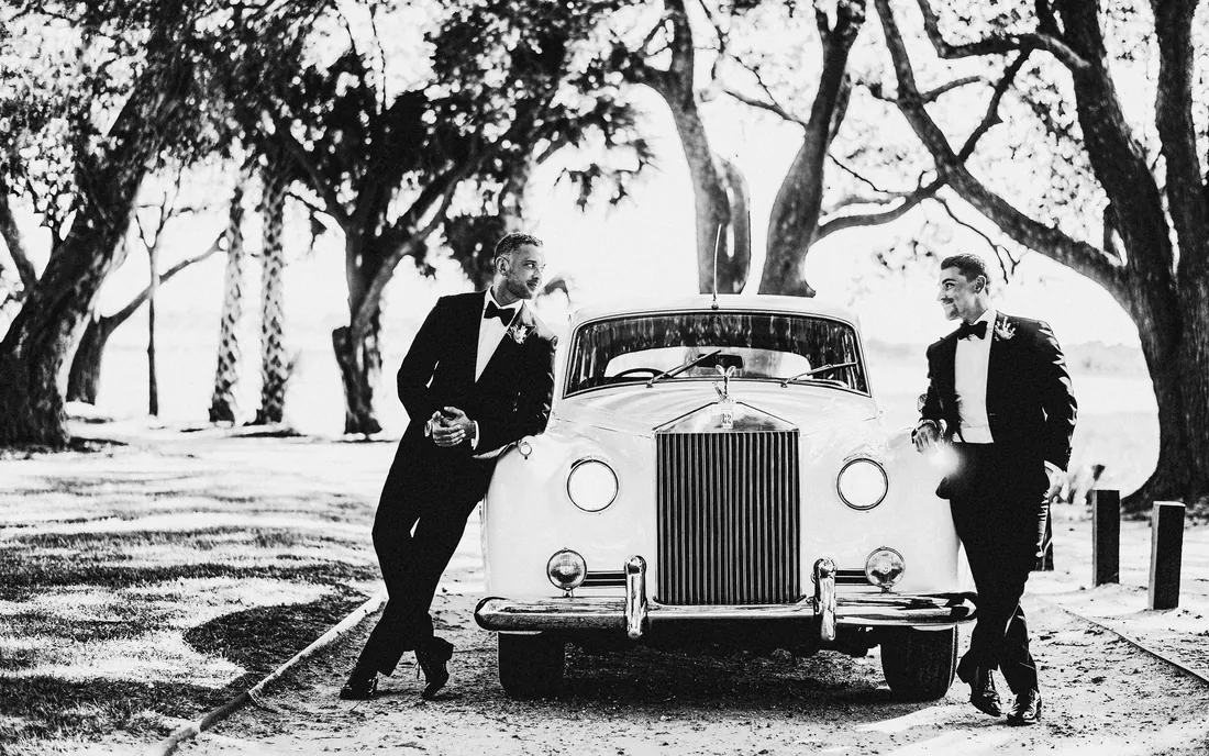 Black and white photo of groomsmen with a vintage car under old trees
