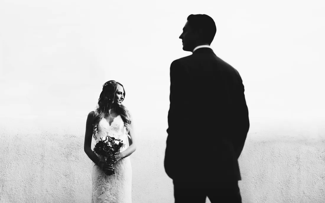 Black and white photo of a bride and groom in silhouette against a bright sky