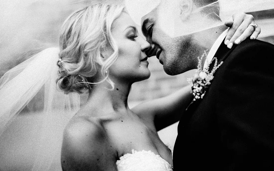 Black and white photo of a bride and groom embracing under her veil