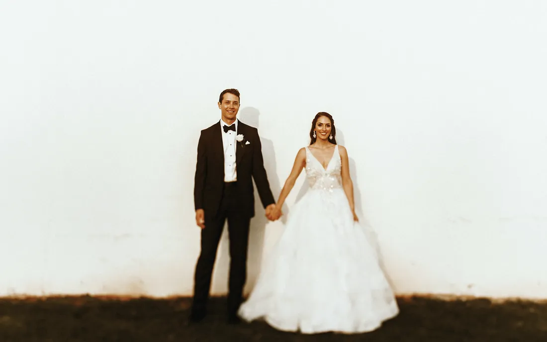 Bride and groom holding hands against a bright white wall