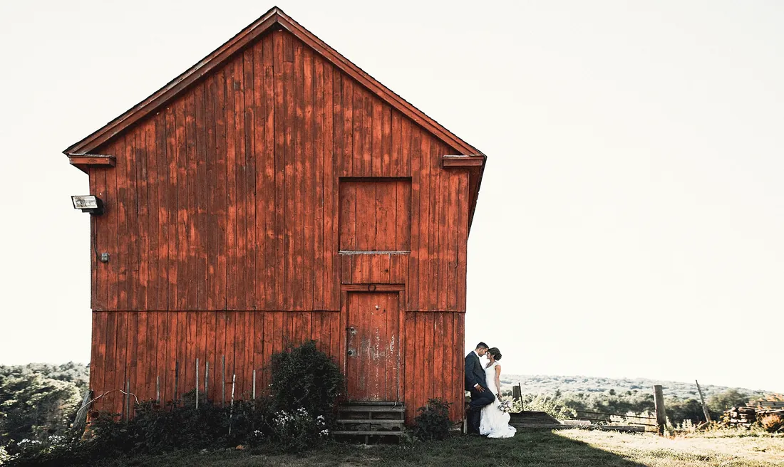 Bride and groom small beside a weathered red barn