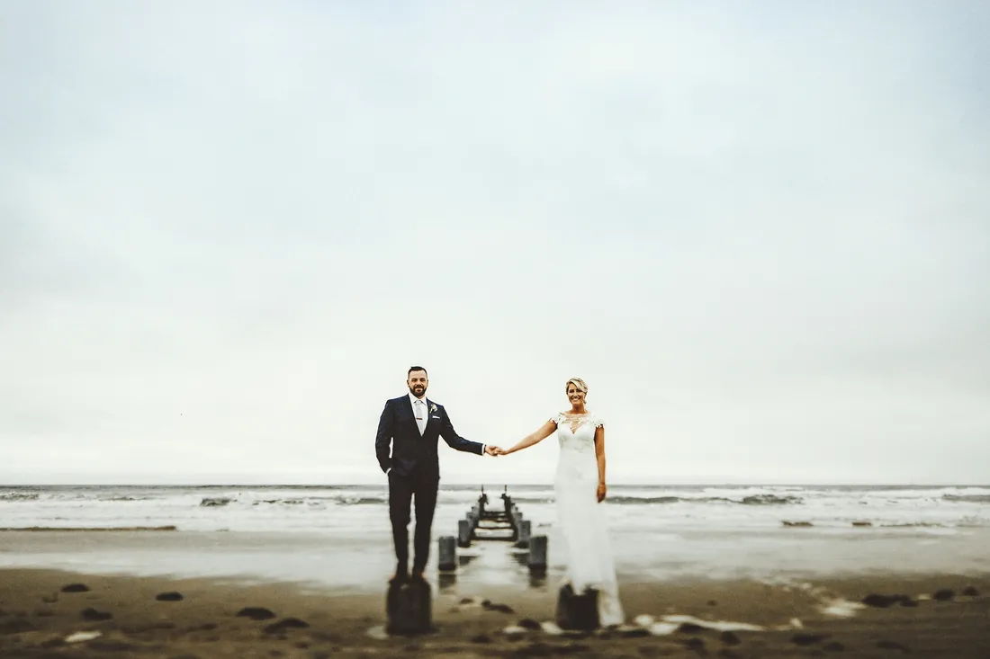 Bride and groom holding hands on the beach beside old pier pilings