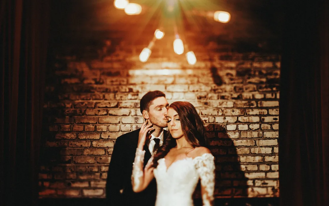 Bride and groom under string lights against a brick wall