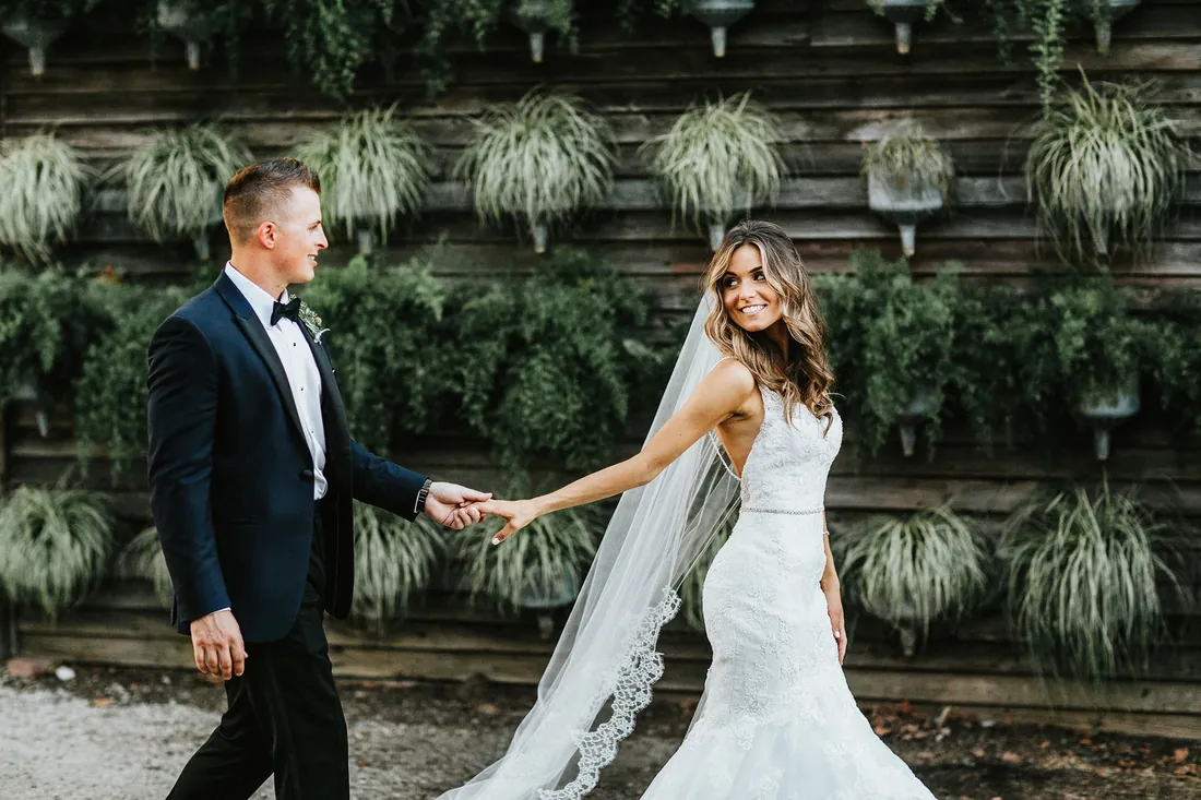 Groom leading his bride by the hand in front of a living plant wall