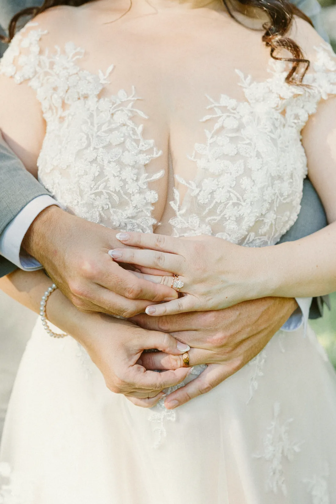 Close-up of a groom's arms wrapped around his bride, their rings together