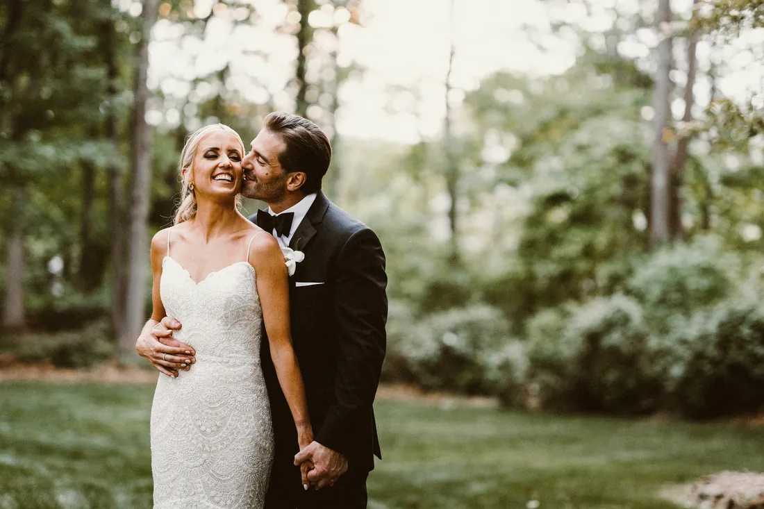 Groom kissing his smiling bride in a green garden
