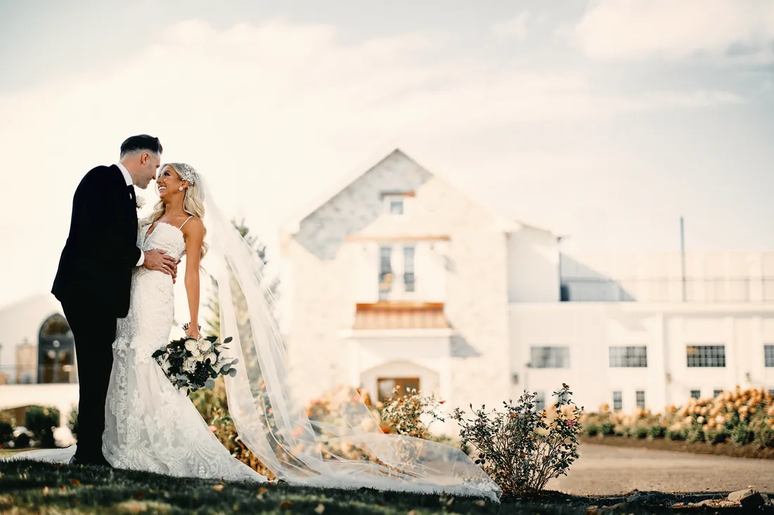 Bride and groom kissing as her long veil trails across the lawn