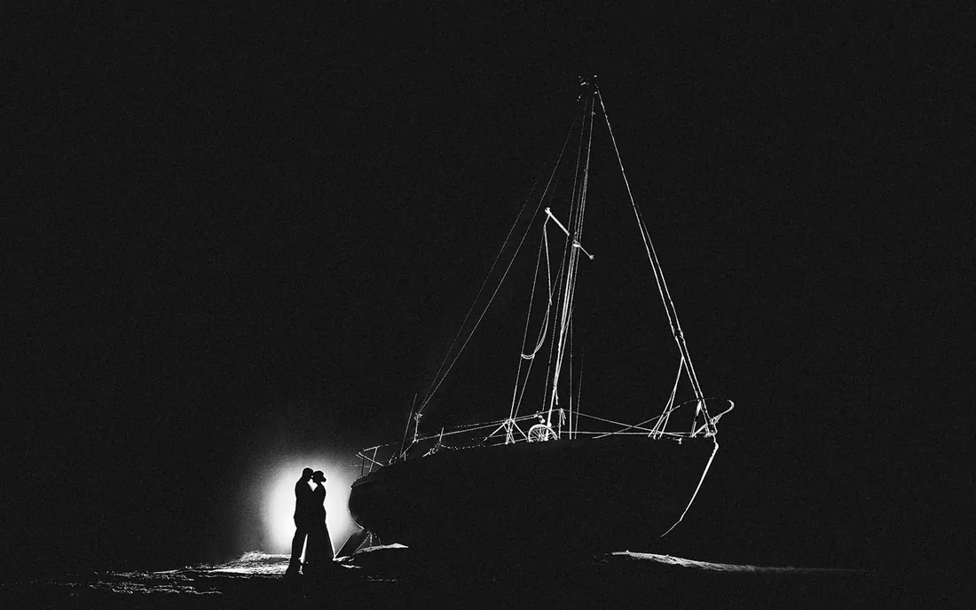 Bride and groom in silhouette beside a sailboat at night