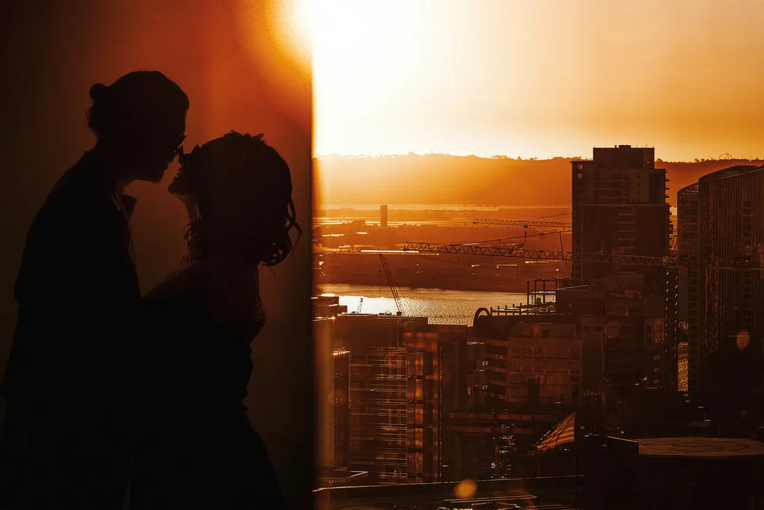 Bride and groom in silhouette over a city at sunset