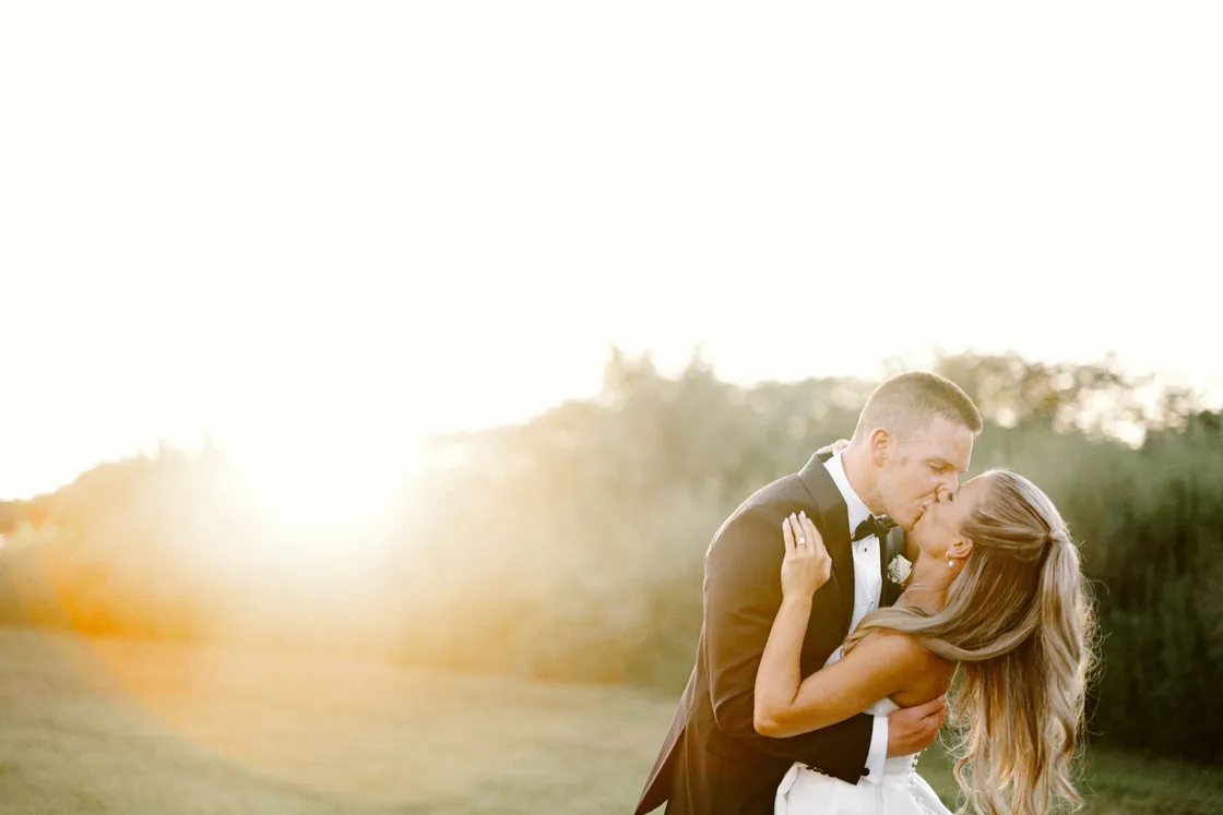 Steve and Madison kissing in golden sunset light at their Bishop Farmstead barn wedding in New Jersey