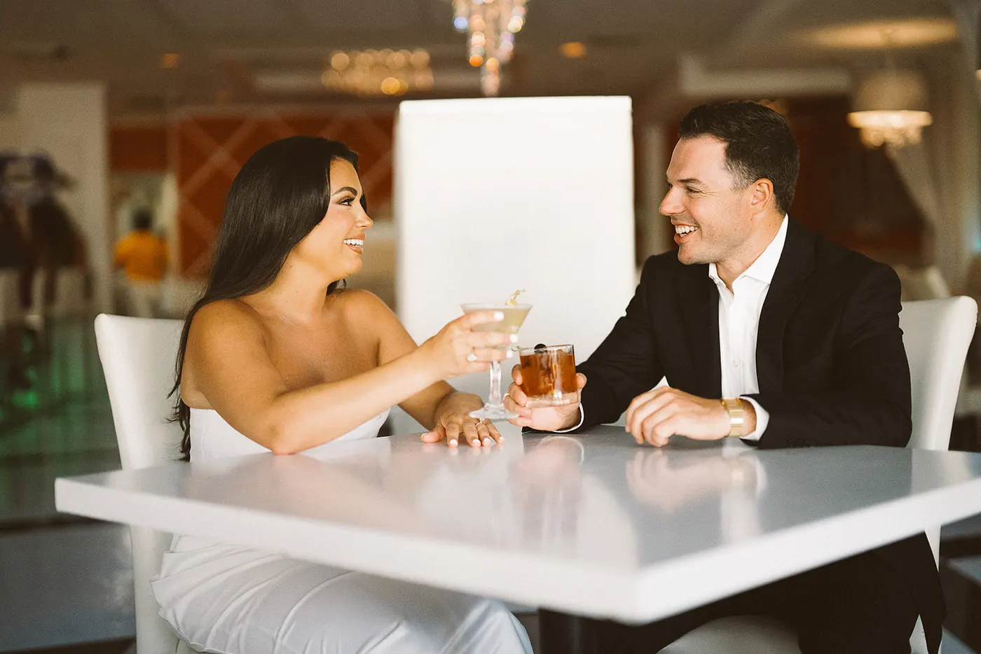 Branon and Celeste toasting with cocktails at a bright white lounge before their Ocean City engagement session