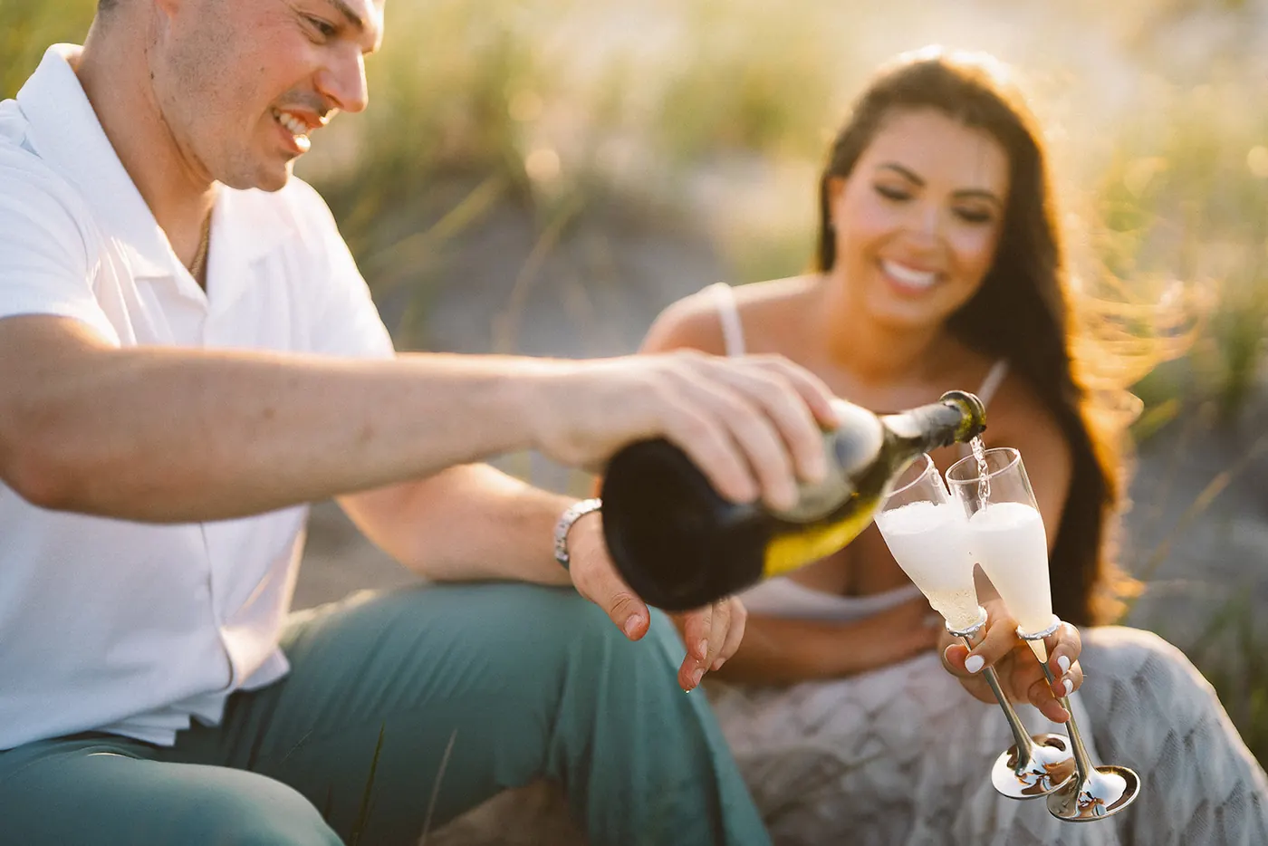 Branon pouring champagne into Celeste's glass in the dune grass