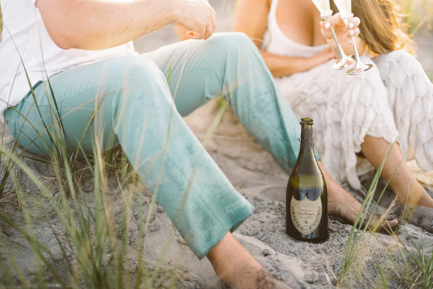 Champagne bottle in the sand beside Branon and Celeste's feet