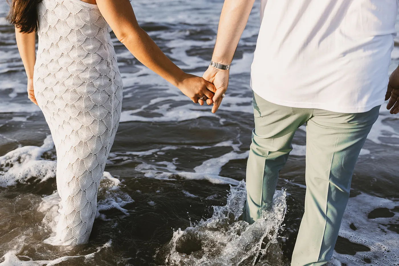 Close-up of Branon and Celeste holding hands as they wade into the surf