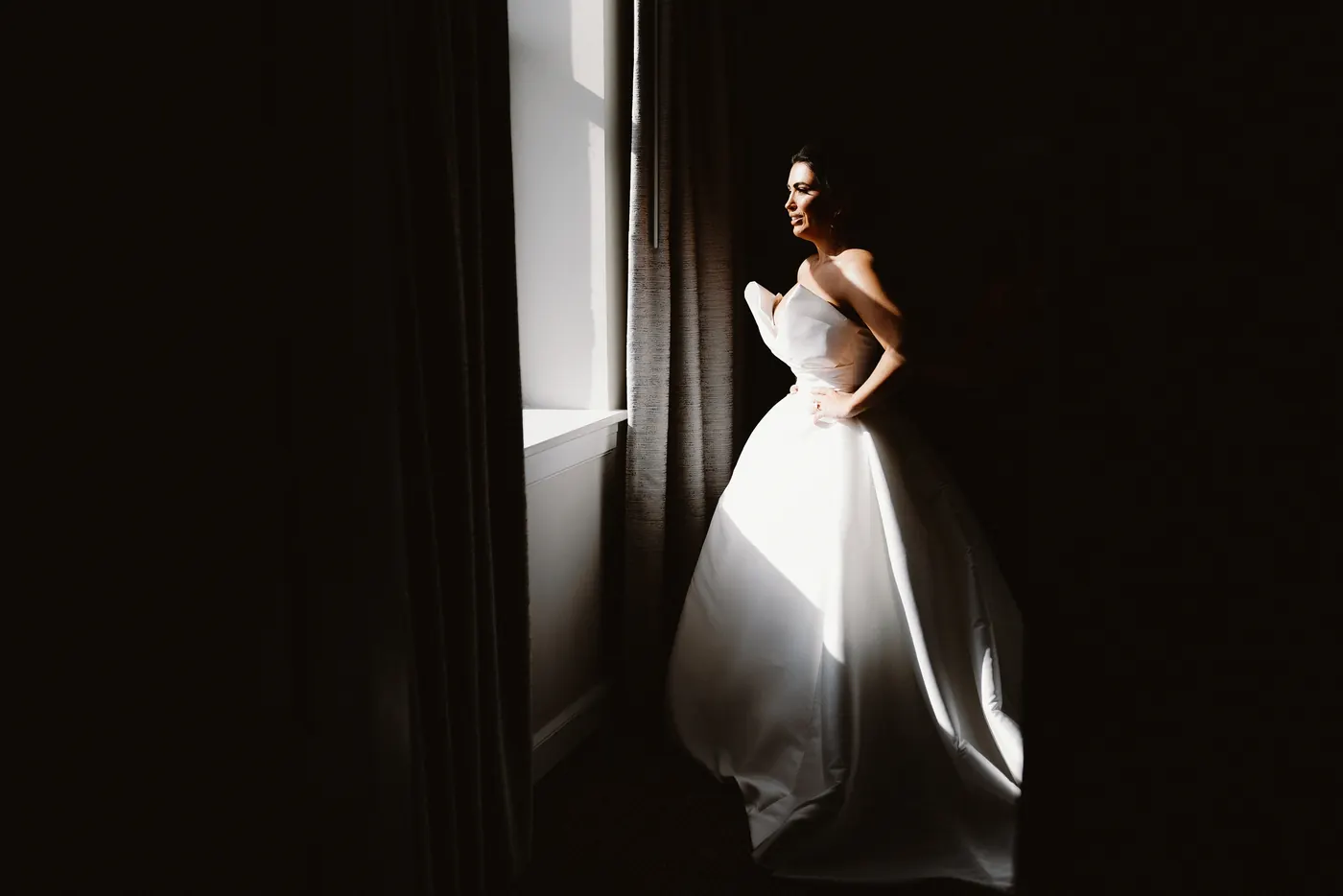 Celeste standing in dramatic window light in her strapless gown
