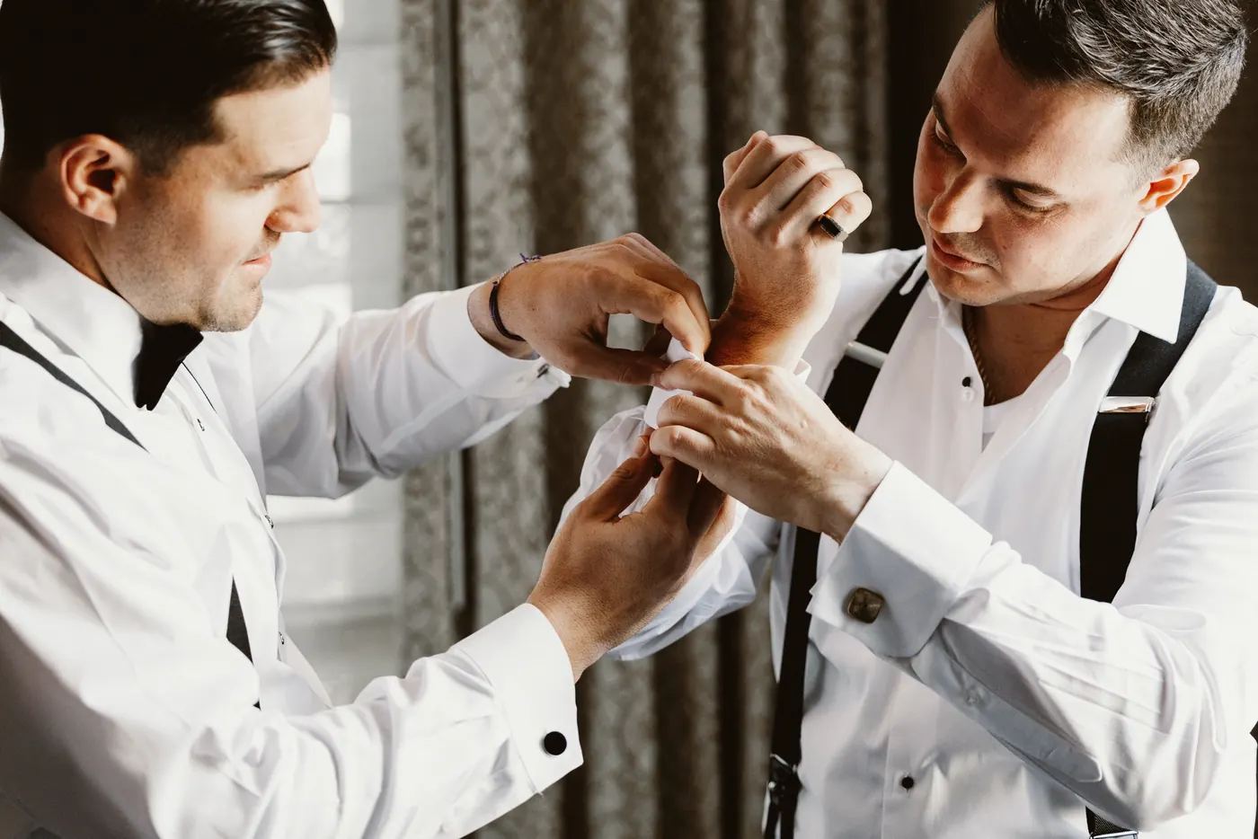 A groomsman helping Branon with his cufflinks
